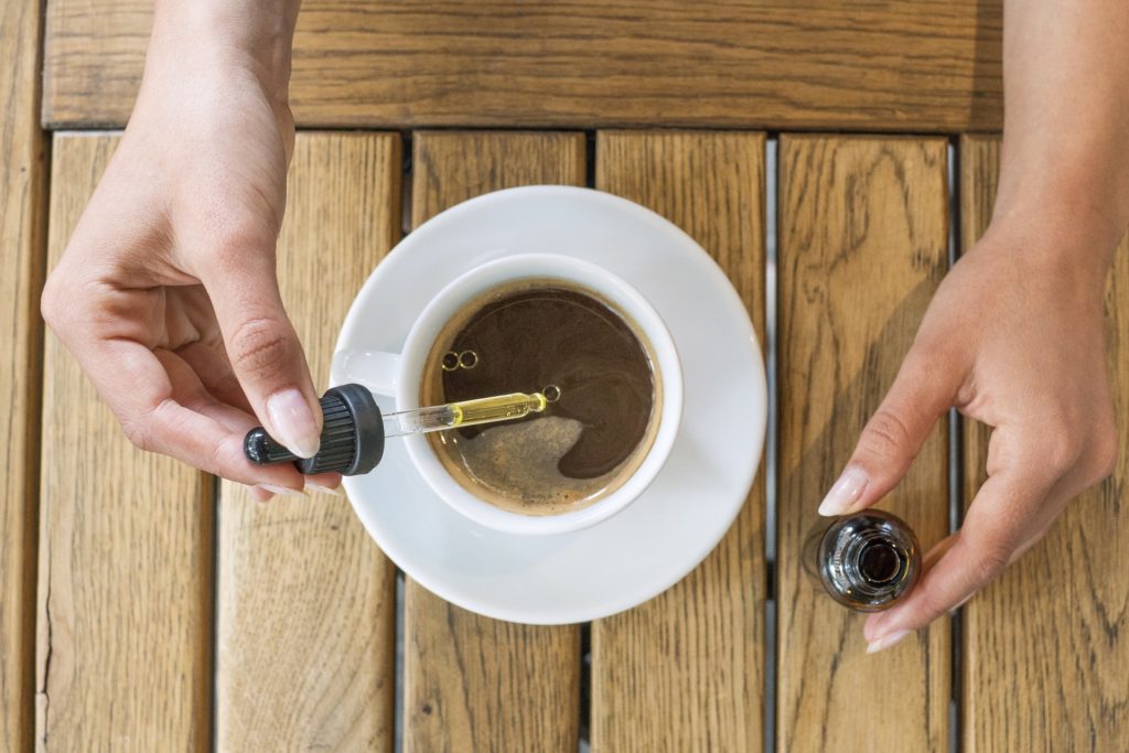 A person adding CBD tincture to coffee