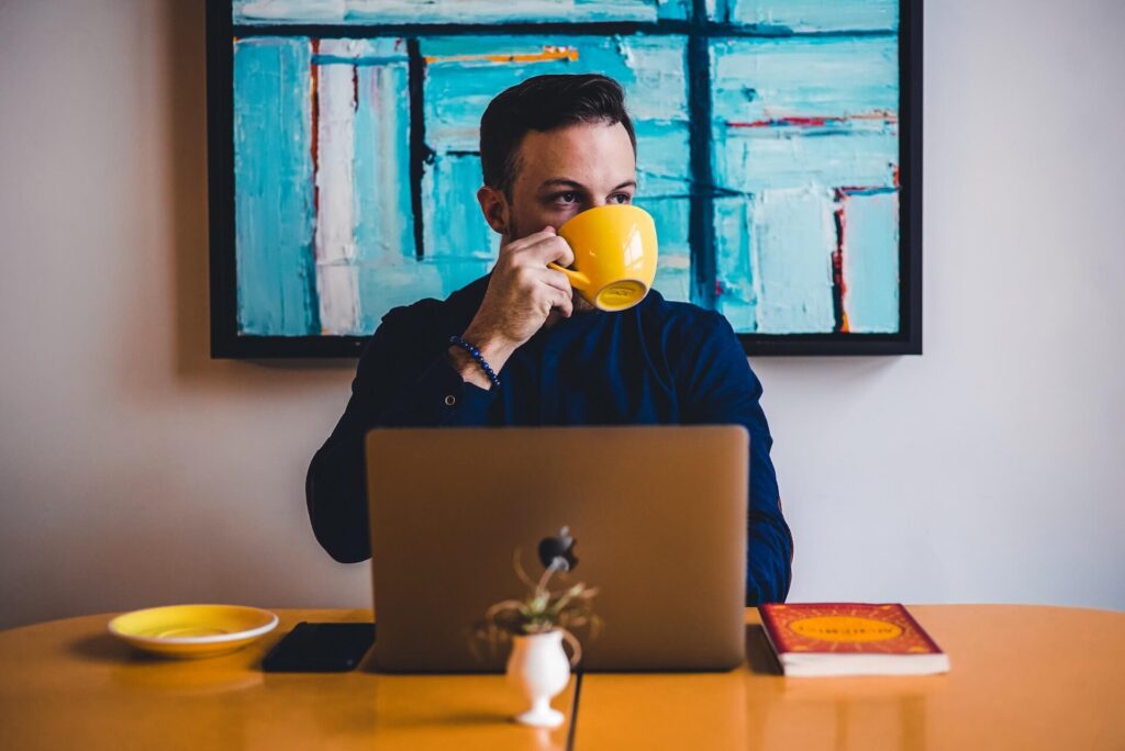 Man sips coffee in yellow mug while at a computer