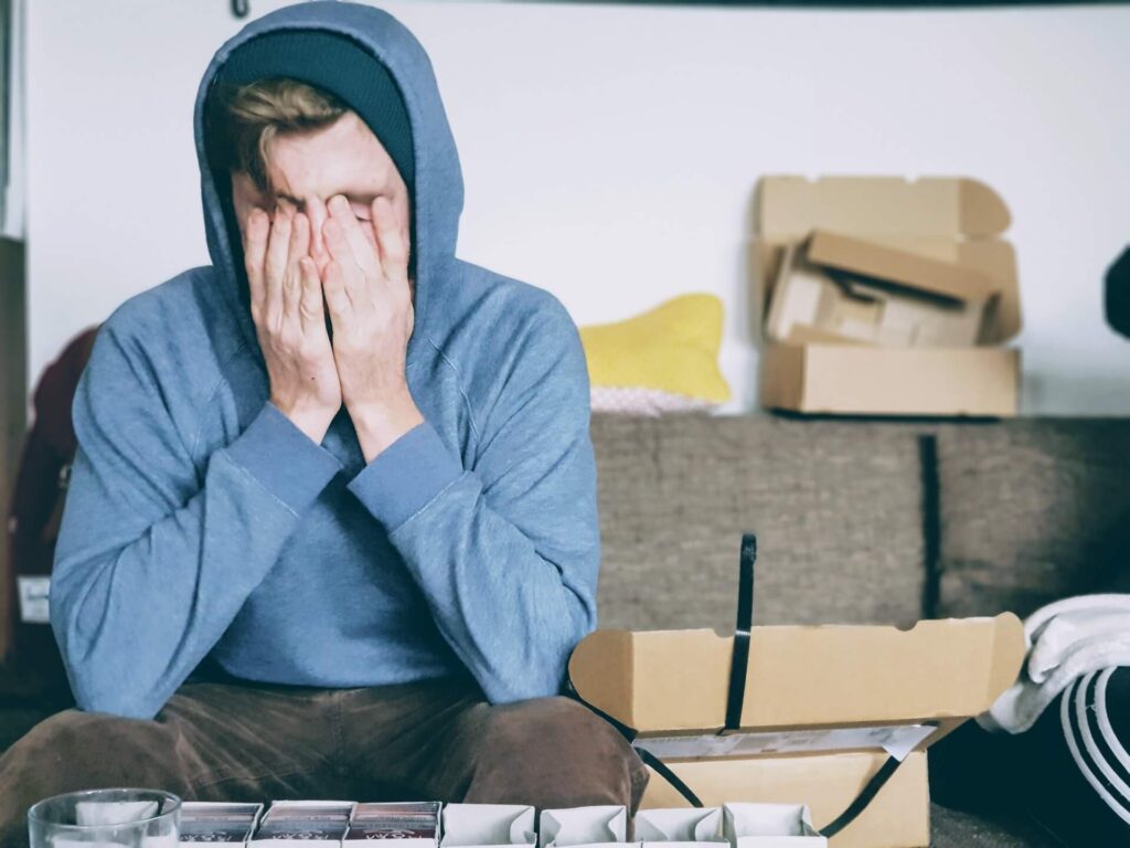 Man in hoodie covers face while unpacking boxes